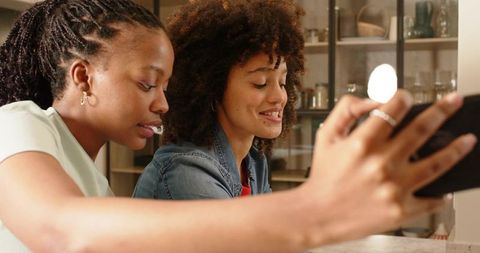 Diverse young women smiling while taking selfie with smartphone and ring light