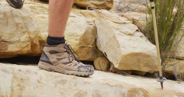 Feet of male survivalist trekking across rocky terrain in walking boots and using walking poles. exploration, travel and adventure, survivalist in the nature.