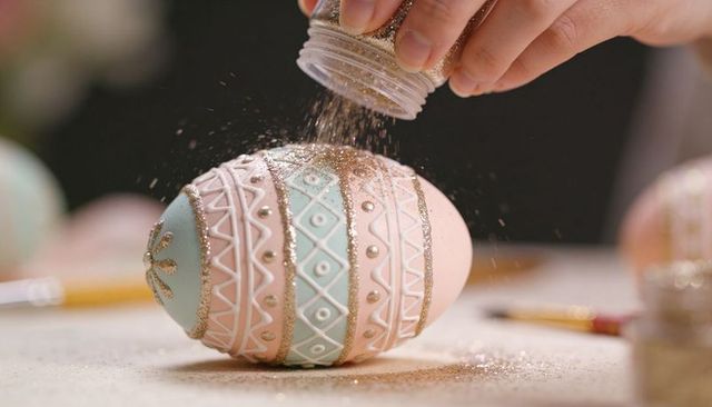 Hand sprinkling gold glitter on pastel easter egg with pearl details