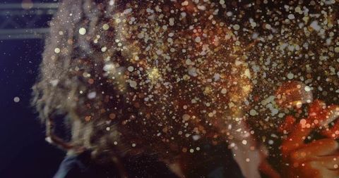 Backlit curly-haired singer performing with microphone amid golden bokeh particles