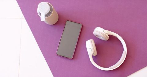 Smartphone sitting on purple mat with headphones and tumbler flatlay