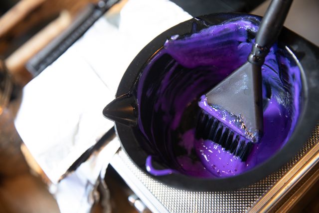 Close up of bowl with purple hair dye, brush and foil prepared for colouring hair in hair salon. Hair and beauty treatment service.