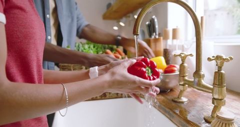 Diverse Couple Washing Bell Pepper in Cozy Kitchen Space