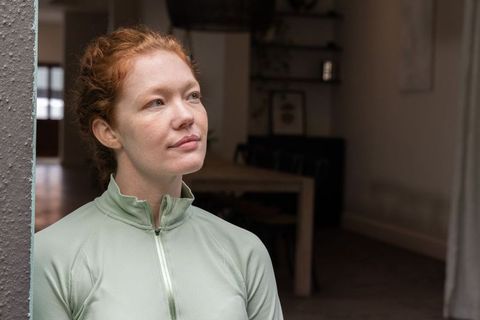 Contemplative redhead woman in 30s leaning by doorway at home with soft natural light