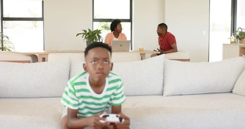 African american family at home boy playing video game on couch while parents working and talking