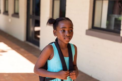 Sunlit african american girl carrying backpack on school walkway portrait back-to-school