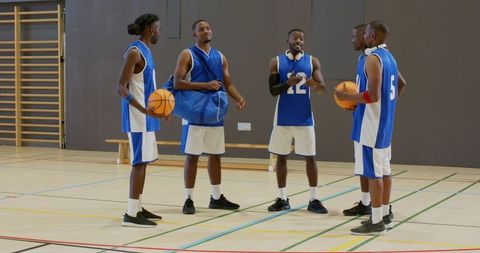 Five basketball players huddling on indoor court wearing blue jerseys preparing for game