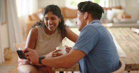 African american couple sharing coffee and laughs while browsing smartphone in cozy home