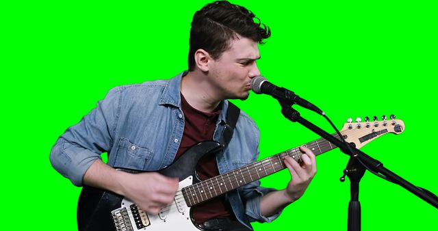 Male musician singing while playing guitar against green screen