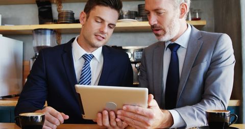 Businessmen Collaborating Over Tablet in Coffee Shop Meeting