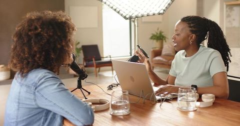 Female Co-hosts Recording Podcast in Modern Home Studio with Laptop and Tabletop Mics