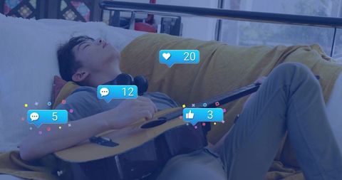 Teenage male napping with guitar and headphones while social media reactions float nearby