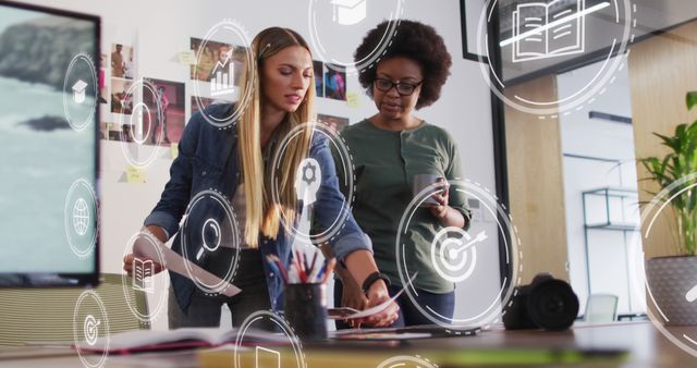 Two Women Collaborating in High-Tech Office with Futuristic Icons - Download Free Stock Images Pikwizard.com