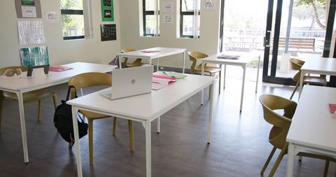 Sunlit modern classroom with laptop on central desk and colorful notebooks