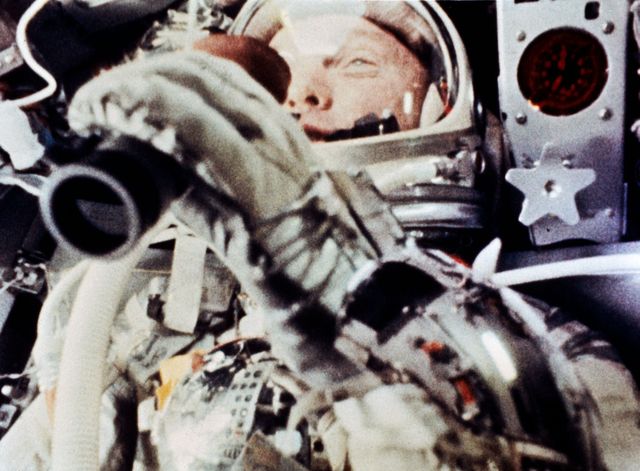 Image captures astronaut using binoculars to observe Earth from the Mercury-Atlas Friendship 7 capsule during an orbital flight. Useful for illustrating early space exploration, highlighting NASA's achievements, and for educational purposes regarding historical space missions.