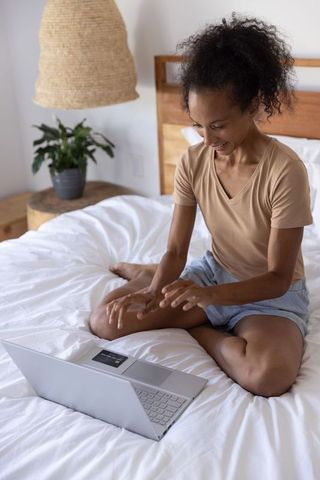 Woman working on laptop in minimalist cozy bedroom for remote work and relaxation