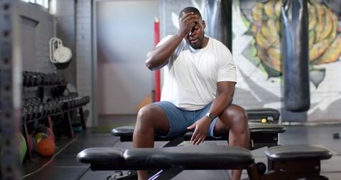 Gym athlete sitting on bench wiping forehead after intense training, resting between sets