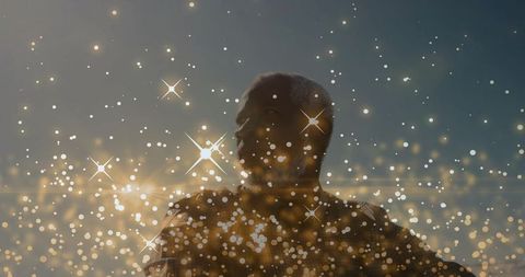 Standing silhouetted man facing dusk with golden bokeh and starburst light flares