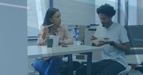 Two coworkers sharing casual lunch and conversation in office breakroom with smartphone