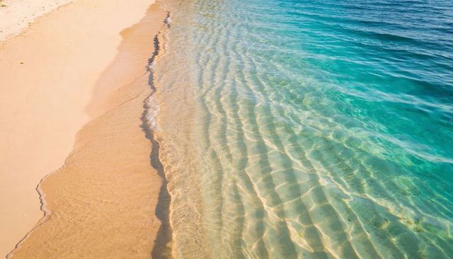 Shimmering turquoise water lapping smooth golden sand with sunlit caustics and ripples