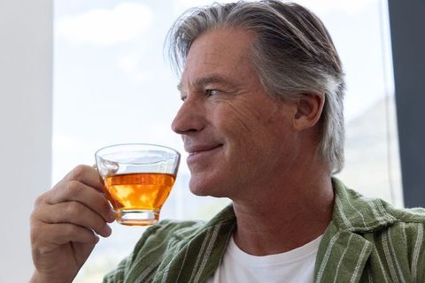 Middle-aged man enjoying tea by window looking relaxed and reflective in sunlit interior