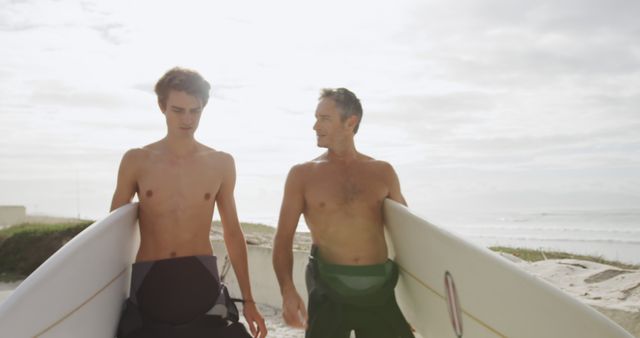 Young Caucasian man and Caucasian man holding surfboards on the beach. They are preparing for a surfing session, enjoying the outdoor coastal environment.
