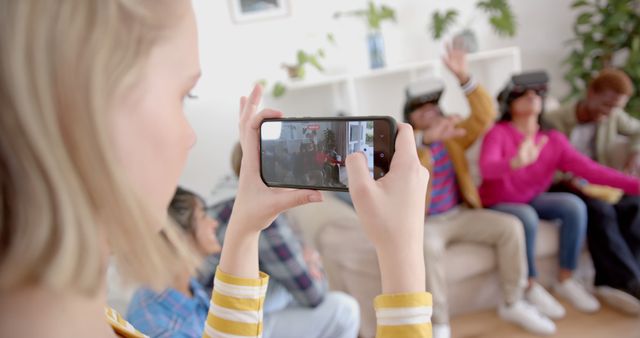 Group of friends in living room enjoying virtual reality technology. Person in foreground taking photo while others in background interacting with VR headsets. Could be used for articles on technology trends, socializing, modern living, and innovative gadgets.