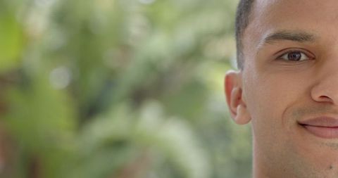 Half-face portrait of man gazing with soft smile and green bokeh background