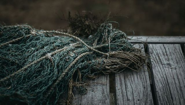 Tangled green fishing net with frayed rope on weathered wooden dock planks