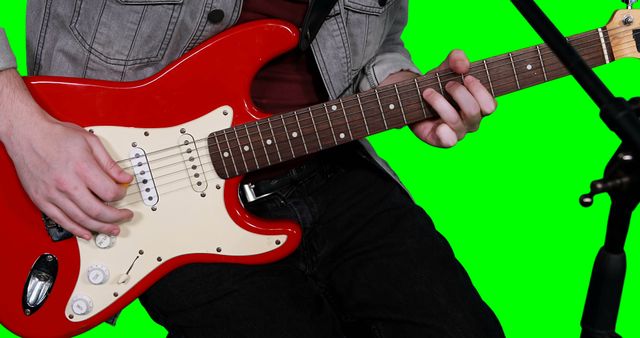 Mid section of male musician playing guitar against green background