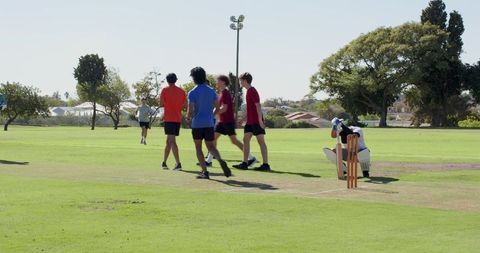 Cricket team walking across grassy pitch adjusting pads and helmet near stumps