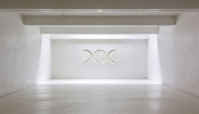Minimalist white gallery featuring triple moon bas-relief under skylight
