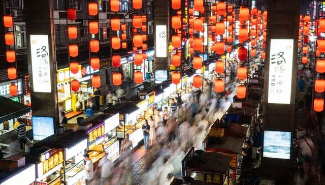 Night market lanterns over busy street food alley with blurred crowds and vendors at night