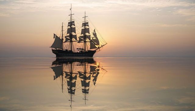 Majestic sailing ship reflecting on tranquil sunrise waters