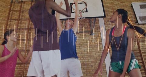 Teen basketball players jumping for rebound under hoop in school gymnasium