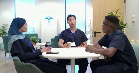 Multicultural medical team chatting and holding coffee in bright staff lounge during break