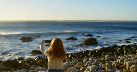 Woman Photographing Ocean at Sunrise on Rocky Beach