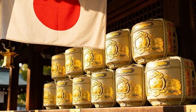 Sunlit sake barrels kazaridaru stacked at shinto shrine with japanese flag and ornate gold crests