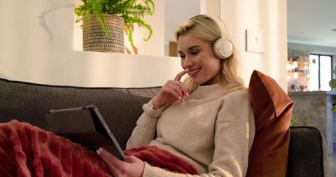 Woman relaxing on sofa with headphones and tablet in cozy modern living room