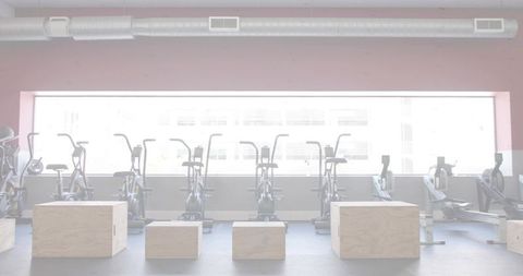 Featuring row of stationary exercise bikes with wooden plyo boxes in bright industrial studio