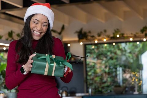 African american woman wearing santa hat smiling opening green christmas gift