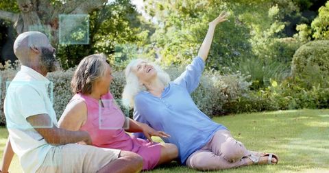 Three friends laughing and relaxing on garden lawn enjoying sunny afternoon together