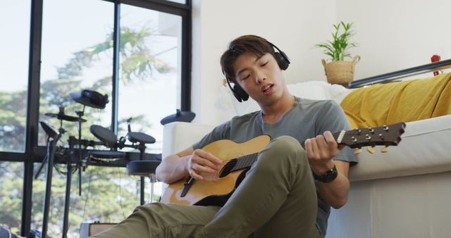 Asian boy wearing headphones playing guitar in living room at home. teenager lifestyle and living concept
