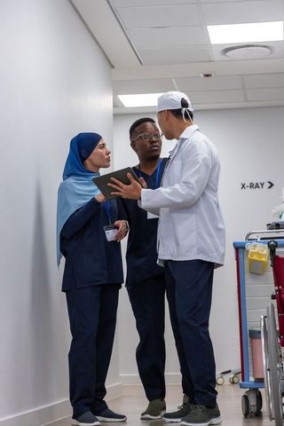 Multicultural medical team collaborating in corridor reviewing tablet near x-ray