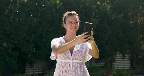 Smiling woman taking selfie in sunlit garden