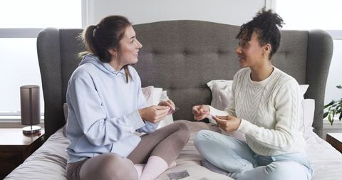 Cozy bedroom bonding: diverse female friends playing cards, laughing and chatting on bed