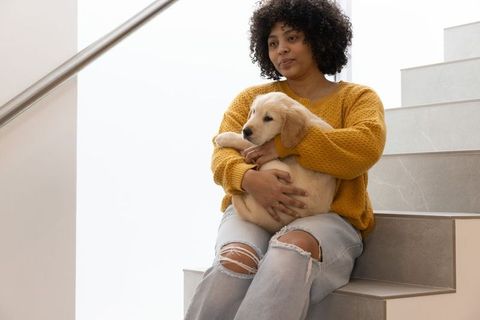 Woman holding golden retriever puppy on staircase wearing yellow sweater and ripped jeans