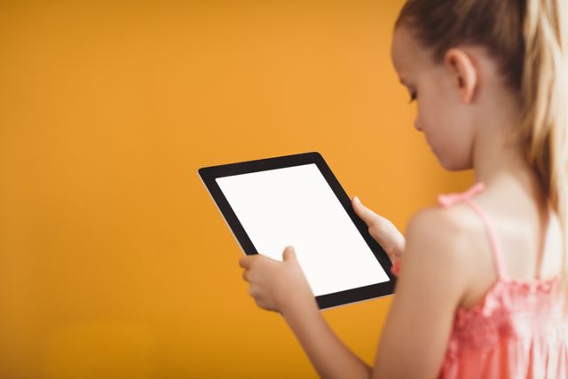 Rear view of girl using a tablet on yellow background