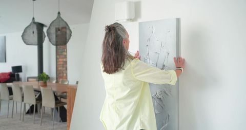 Woman hanging textured canvas on wall in modern open-plan living room decorating home