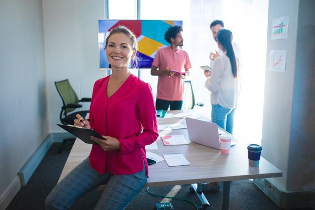 Businesswoman smiling while leading a team meeting in a modern office. Ideal for use in articles about leadership, teamwork, corporate culture, and professional environments. Suitable for business presentations, corporate websites, and promotional materials highlighting collaborative workspaces.